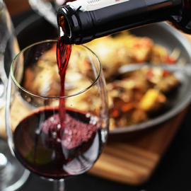 bottle pouring red wine into glass in front of plate of food