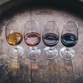 four glasses of wine lined up on a wine barrel