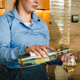 server pouring white wine into wine glass